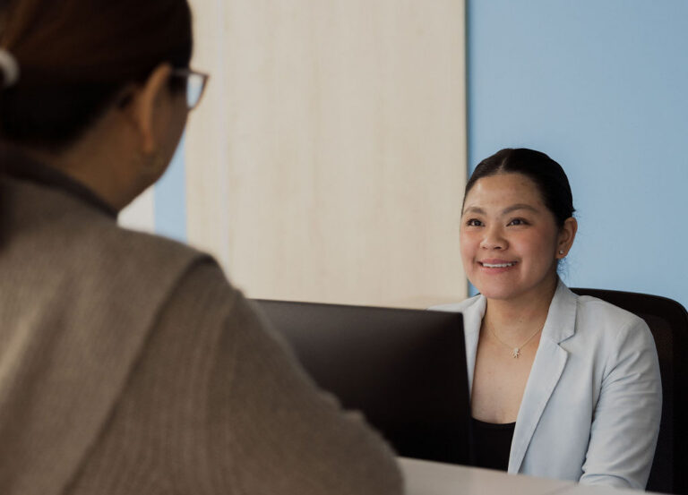 Patient Inquiring with Staff Seating on Desk